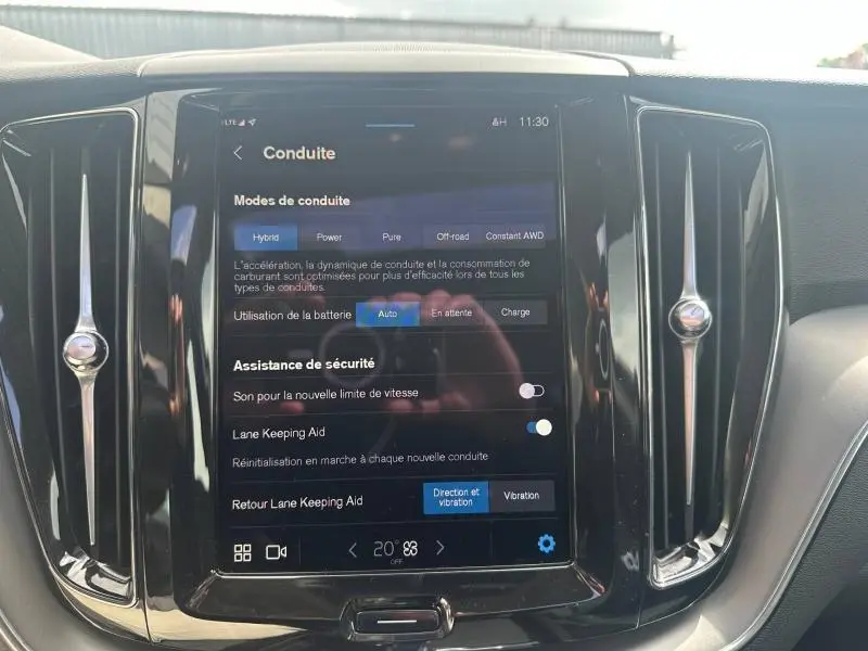 Vue rapprochée de l’écran tactile central noir du Volvo XC60 gris 2024, affichant les modes de conduite et aides à la sécurité.