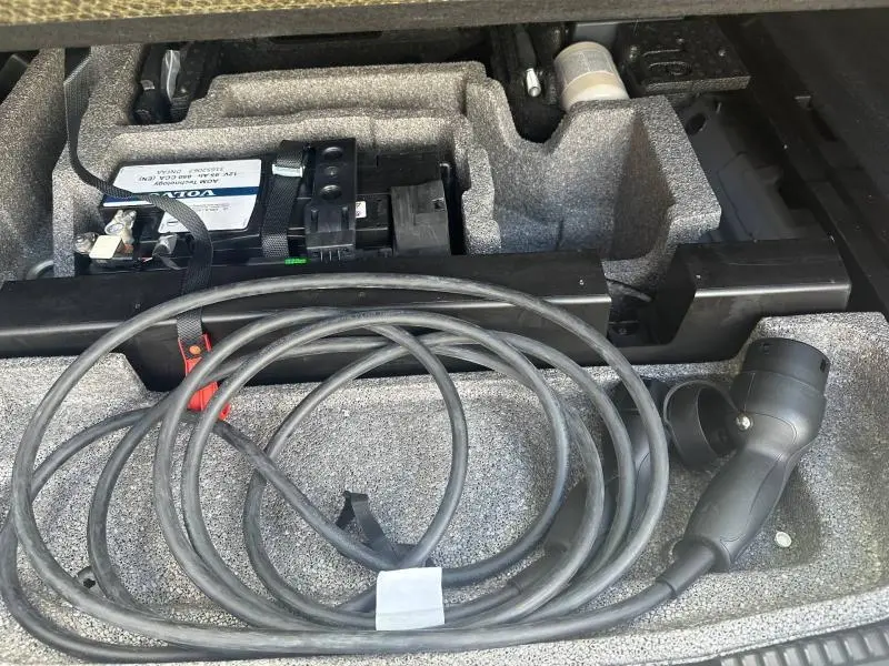 Câble de recharge noir rangé dans le coffre avec batterie visible, intérieur gris du Volvo XC60 hybride rechargeable 2024.