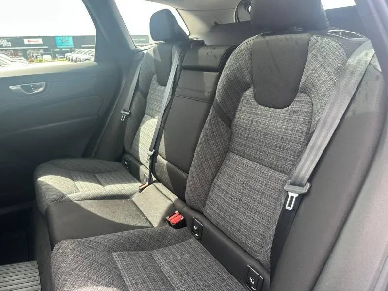 Vue intérieure des sièges arrière gris à motifs du Volvo XC60 2024, avec ceintures de sécurité et habillage de porte visible.