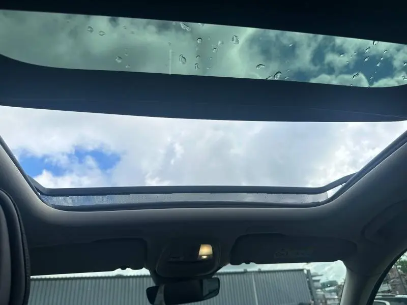 Vue intérieure du toit panoramique ouvert du Volvo XC60 gris 2024, avec ciel nuageux visible à travers la vitre.