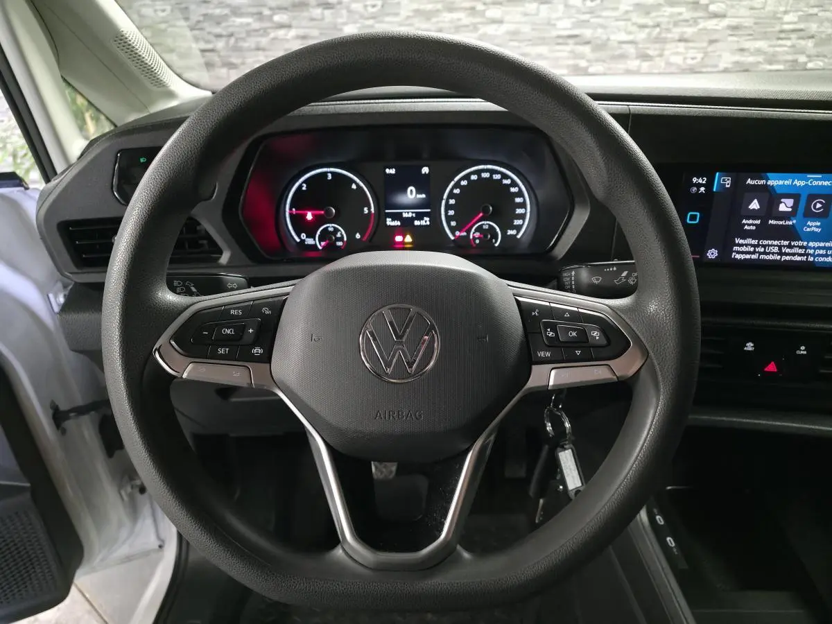 Vue rapprochée du volant multifonction noir et du tableau de bord numérique du Volkswagen Caddy Cargo blanc 2023.