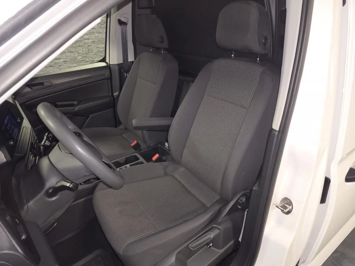 Vue intérieure côté conducteur du Volkswagen Caddy Cargo blanc 2023, sièges tissu gris avec accoudoir et planche de bord noire.