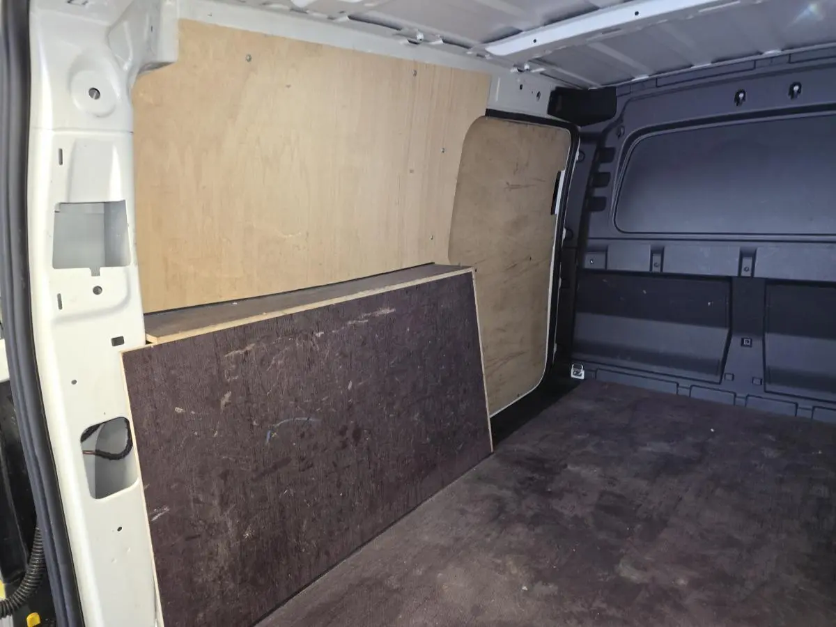 Vue intérieure du compartiment de charge du Volkswagen Caddy Cargo blanc, avec revêtement bois et caoutchouc au sol.