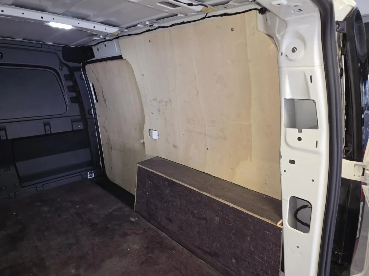 Vue intérieure du compartiment de charge du Volkswagen Caddy Cargo blanc, avec revêtement bois et tapis caoutchouc au sol.