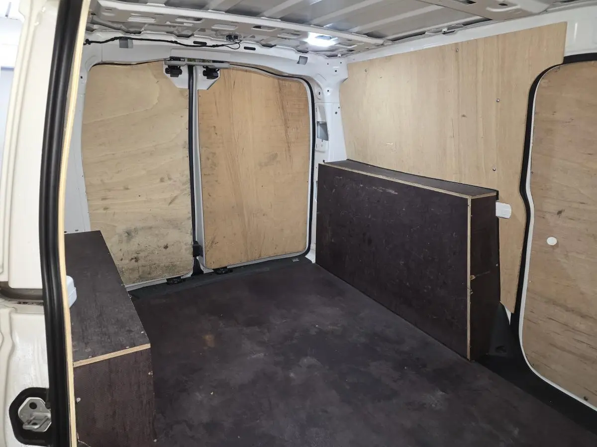 Vue intérieure arrière du fourgon blanc Volkswagen Caddy Cargo 2023, montrant le compartiment de charge avec revêtement bois.