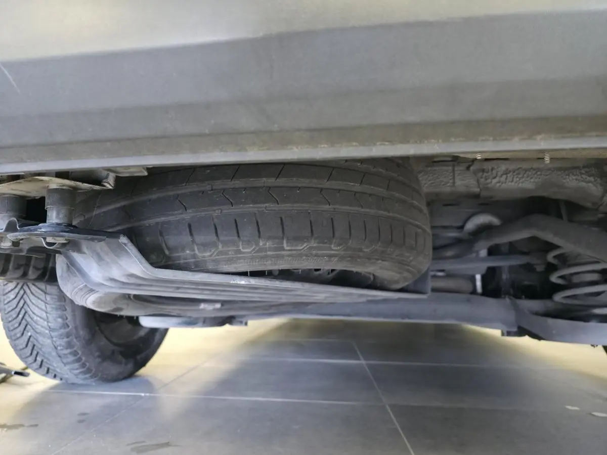 Vue en contre-plongée sous un Volkswagen Caddy blanc montrant la roue de secours et la suspension arrière.
