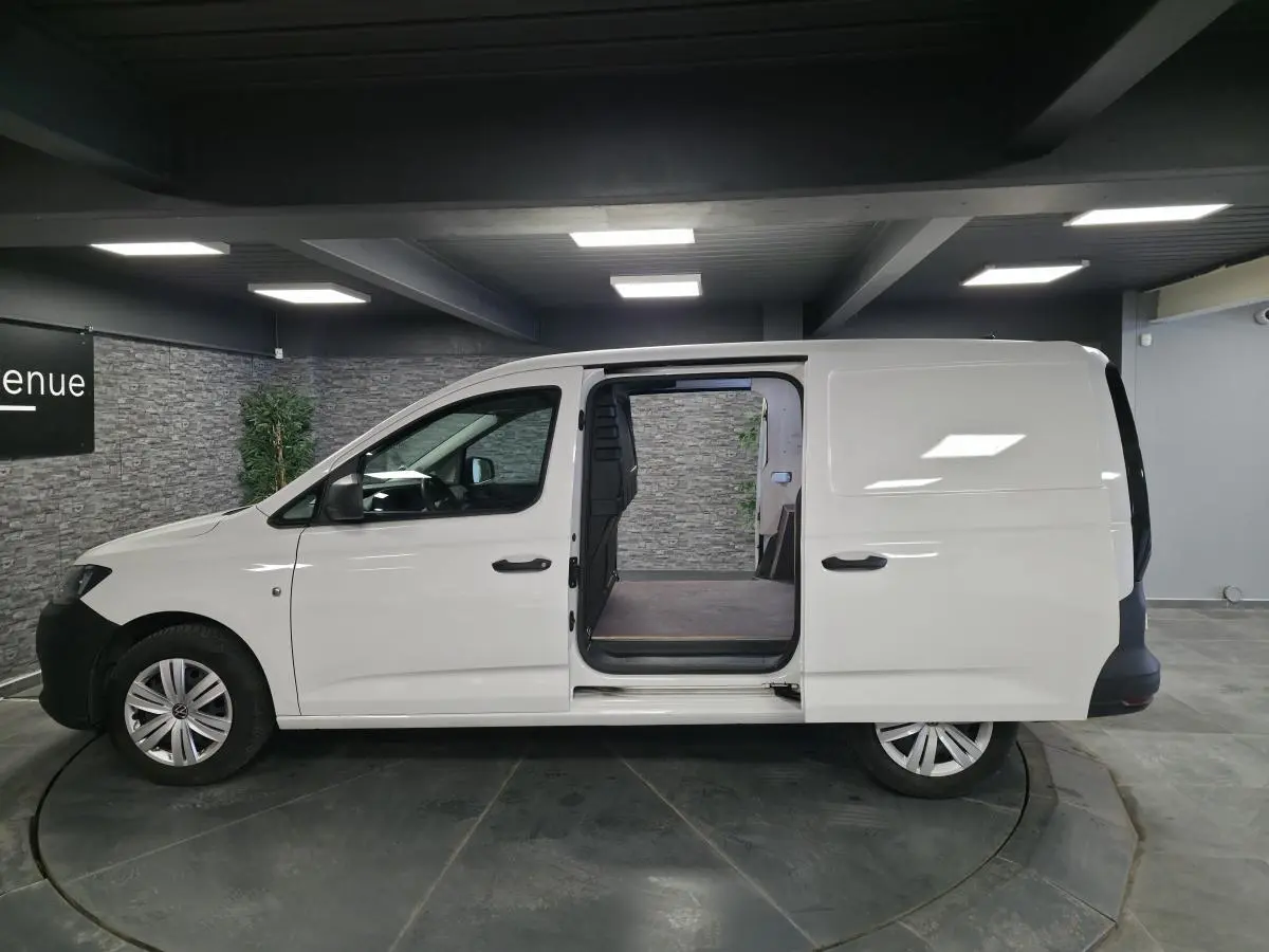 Vue de profil droit d’un utilitaire Volkswagen Caddy Cargo blanc avec porte coulissante ouverte sur le compartiment de charge.
