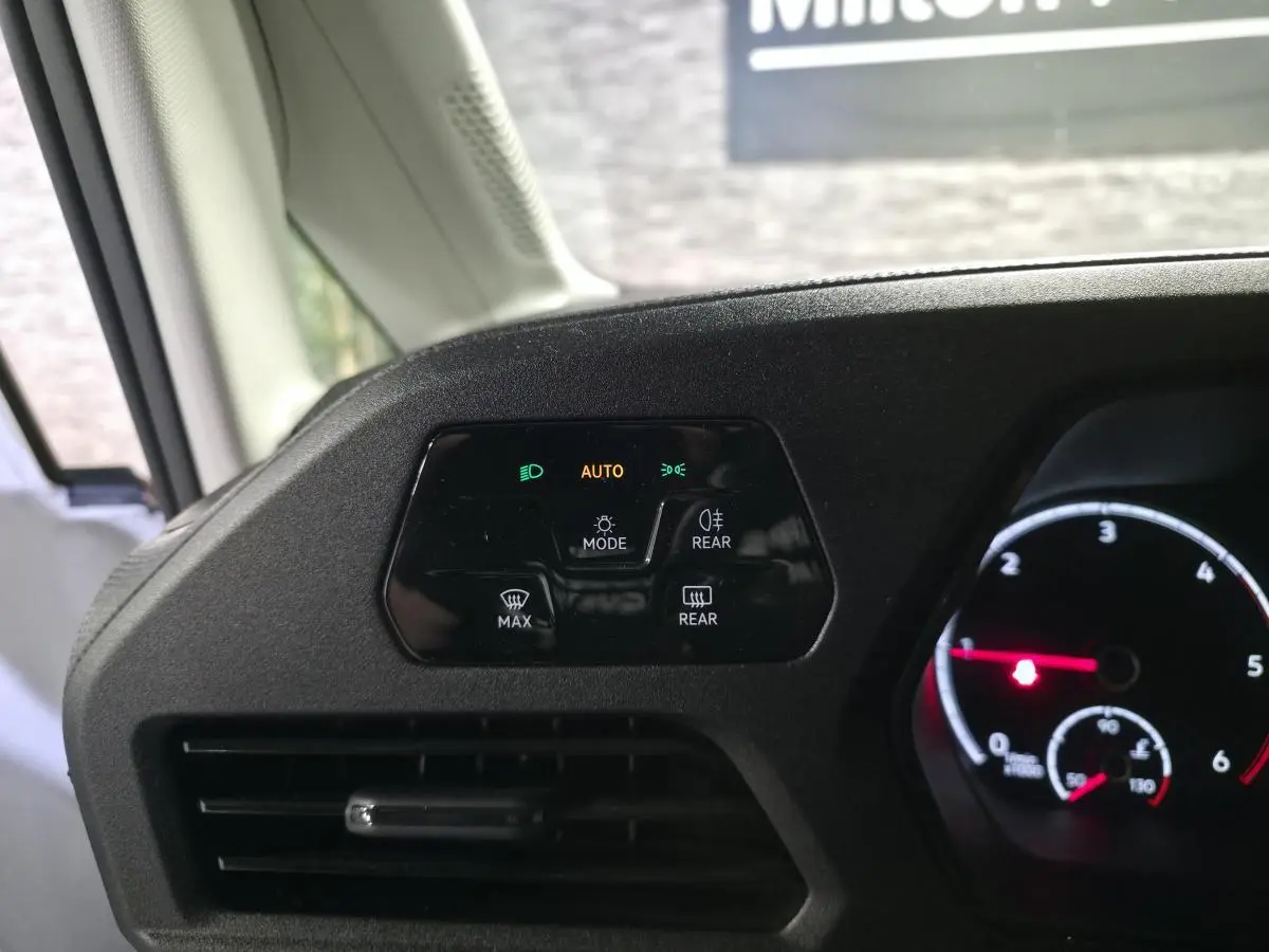Détail du tableau de bord noir mat du Volkswagen Caddy 2023 avec commandes d'éclairage et ventilation côté conducteur.