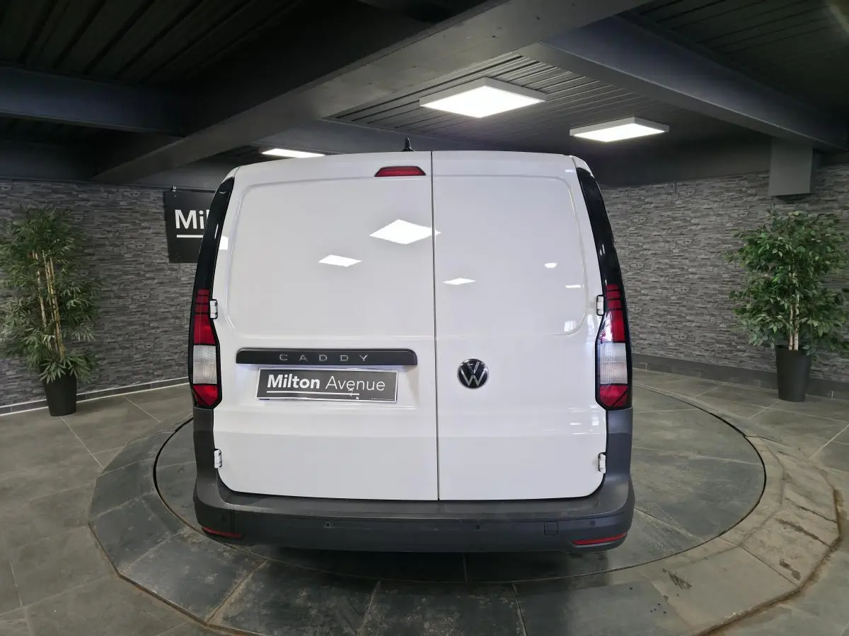 Vue arrière d'un Volkswagen Caddy Cargo blanc 2023 avec portes battantes et pare-chocs noirs dans un showroom.
