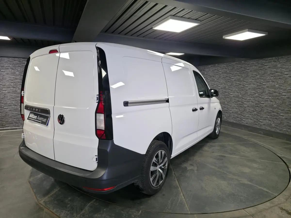 Vue 3/4 arrière droite d'un Volkswagen Caddy Cargo blanc avec portes battantes arrière et jantes en acier noires.