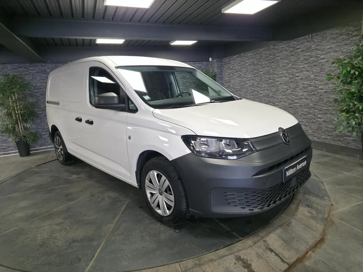 Volkswagen Caddy Cargo blanc en 3/4 avant droit avec pare-chocs noirs et jantes acier en intérieur showroom.