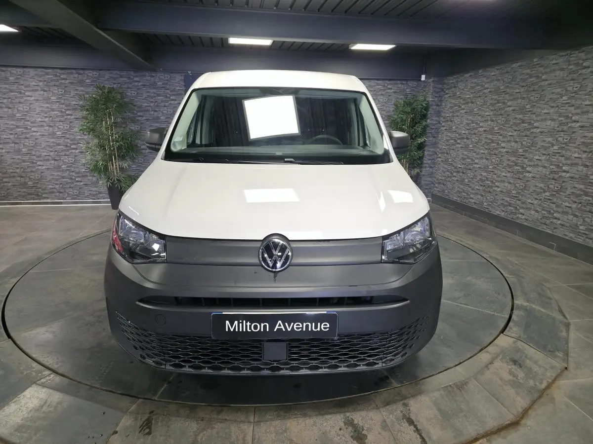 Vue avant d'un Volkswagen Caddy Cargo blanc avec pare-chocs noir mat dans un showroom intérieur.