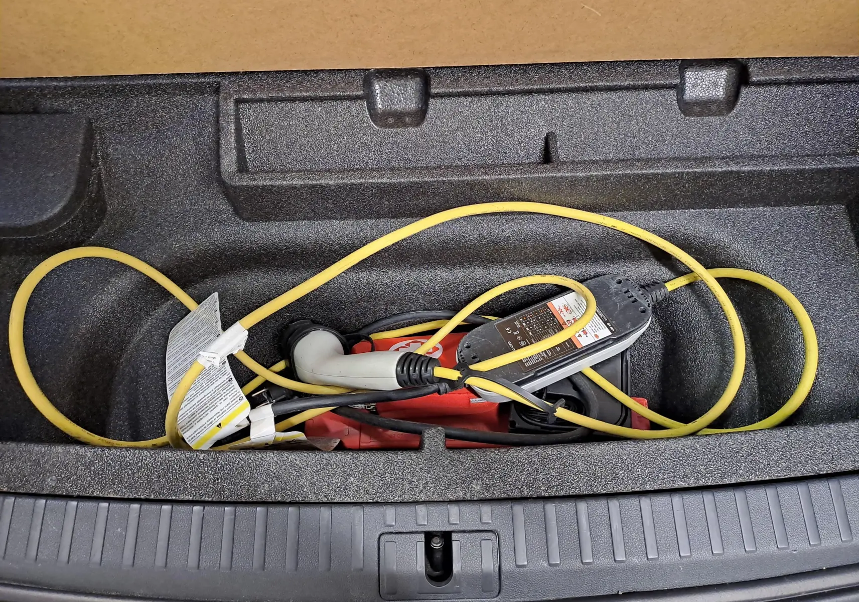 Gros plan sur le compartiment de coffre d'une Skoda Octavia Combi gris perle, montrant le câble de recharge hybride rangé.