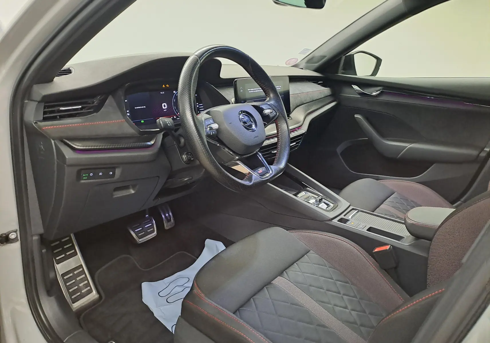 Vue intérieure côté conducteur de la Skoda Octavia Combi 1.4 TSI PHEV 2021 avec sièges noirs et surpiqûres rouges.