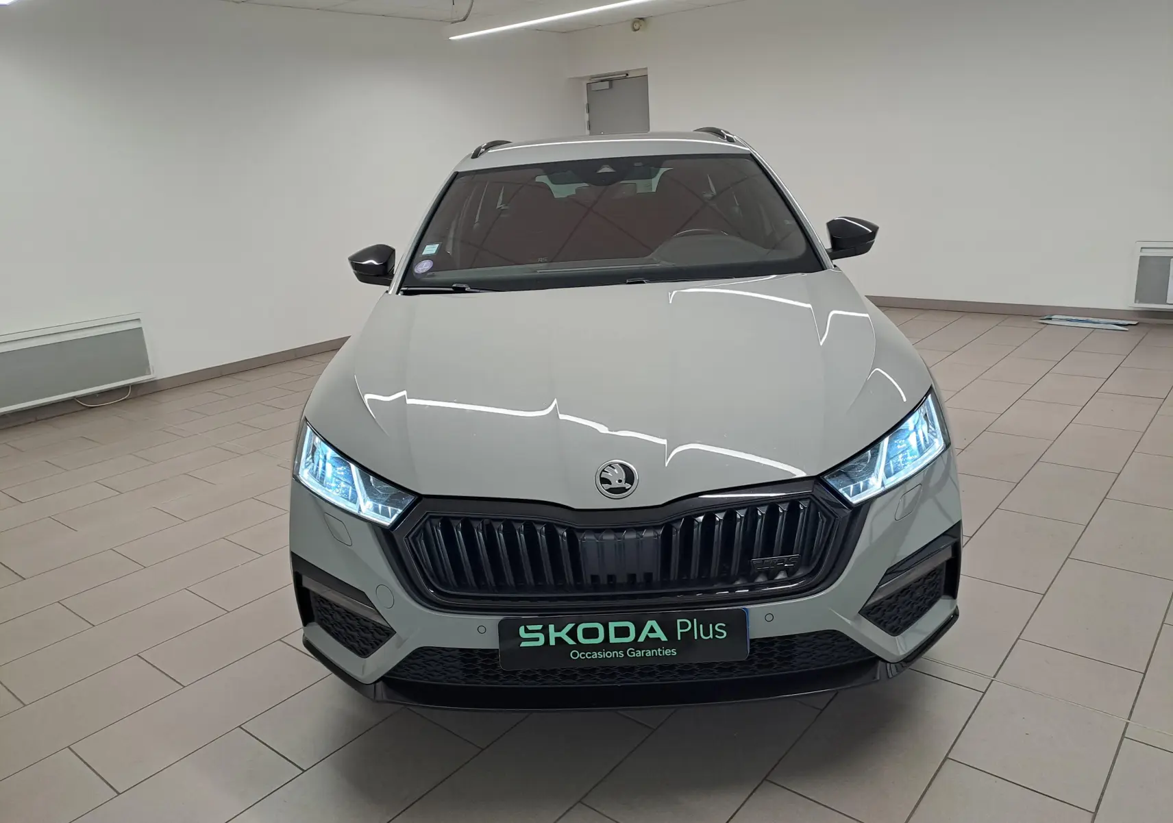 Vue avant d'une Skoda Octavia Combi 1.4 TSI PHEV 245ch gris perle avec phares allumés en intérieur showroom.