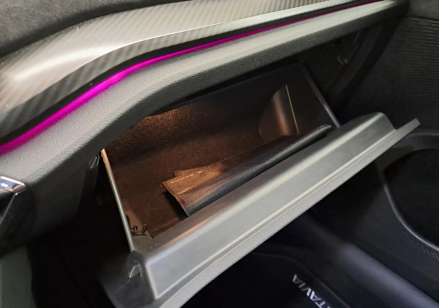 Gros plan sur la boîte à gants ouverte de la Skoda Octavia Combi 1.4 TSI PHEV 245ch RS, avec éclairage intérieur violet.