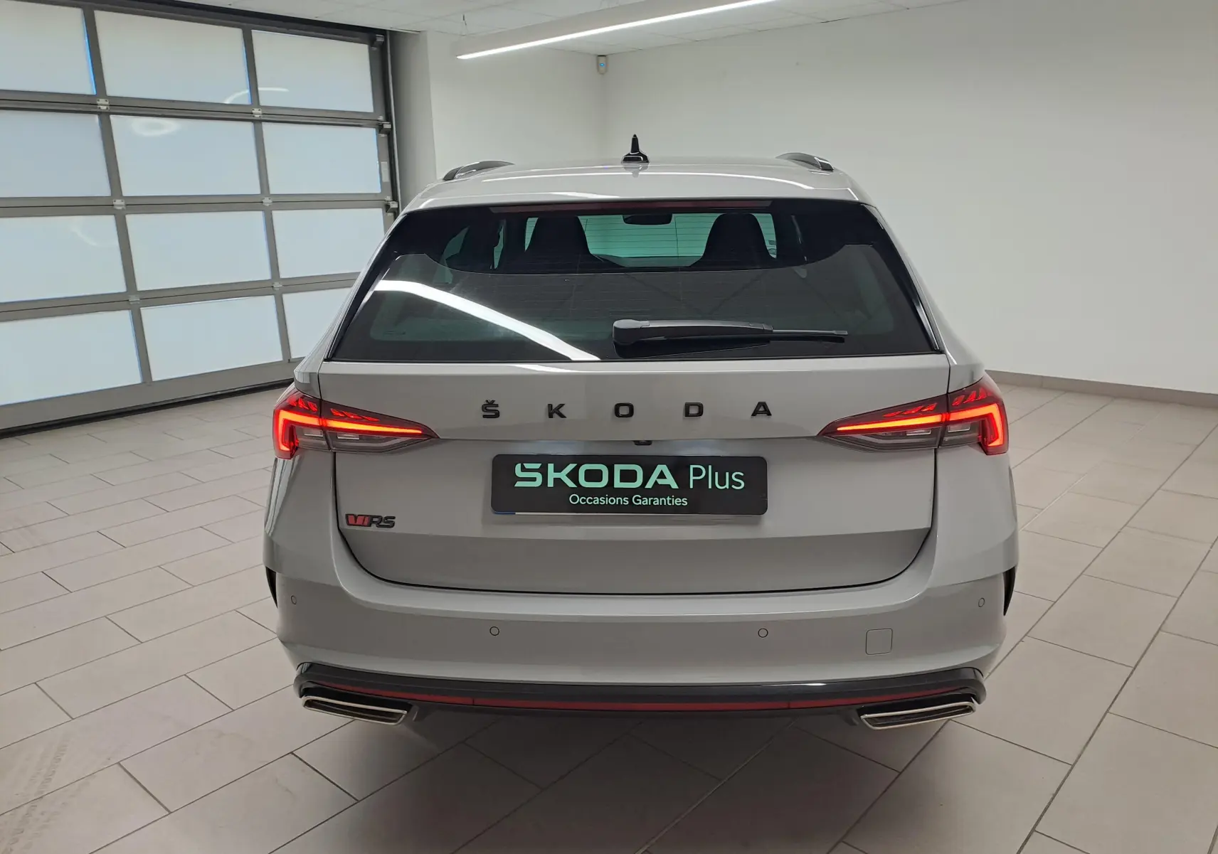 Vue arrière d’une Skoda Octavia Combi RS gris perle avec feux allumés et double sortie d’échappement chromée.