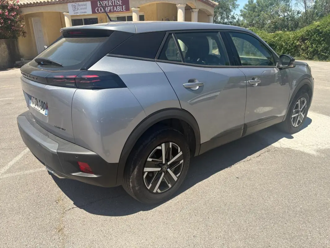 Vue 3/4 arrière droite d’un Peugeot 2008 Hybrid gris 2025 avec jantes 16 pouces et toit noir contrasté.