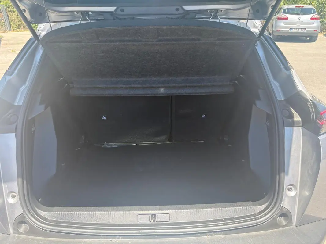 Coffre ouvert en vue arrière du Peugeot 2008 Hybrid 145 gris, mettant en valeur l’espace de chargement.