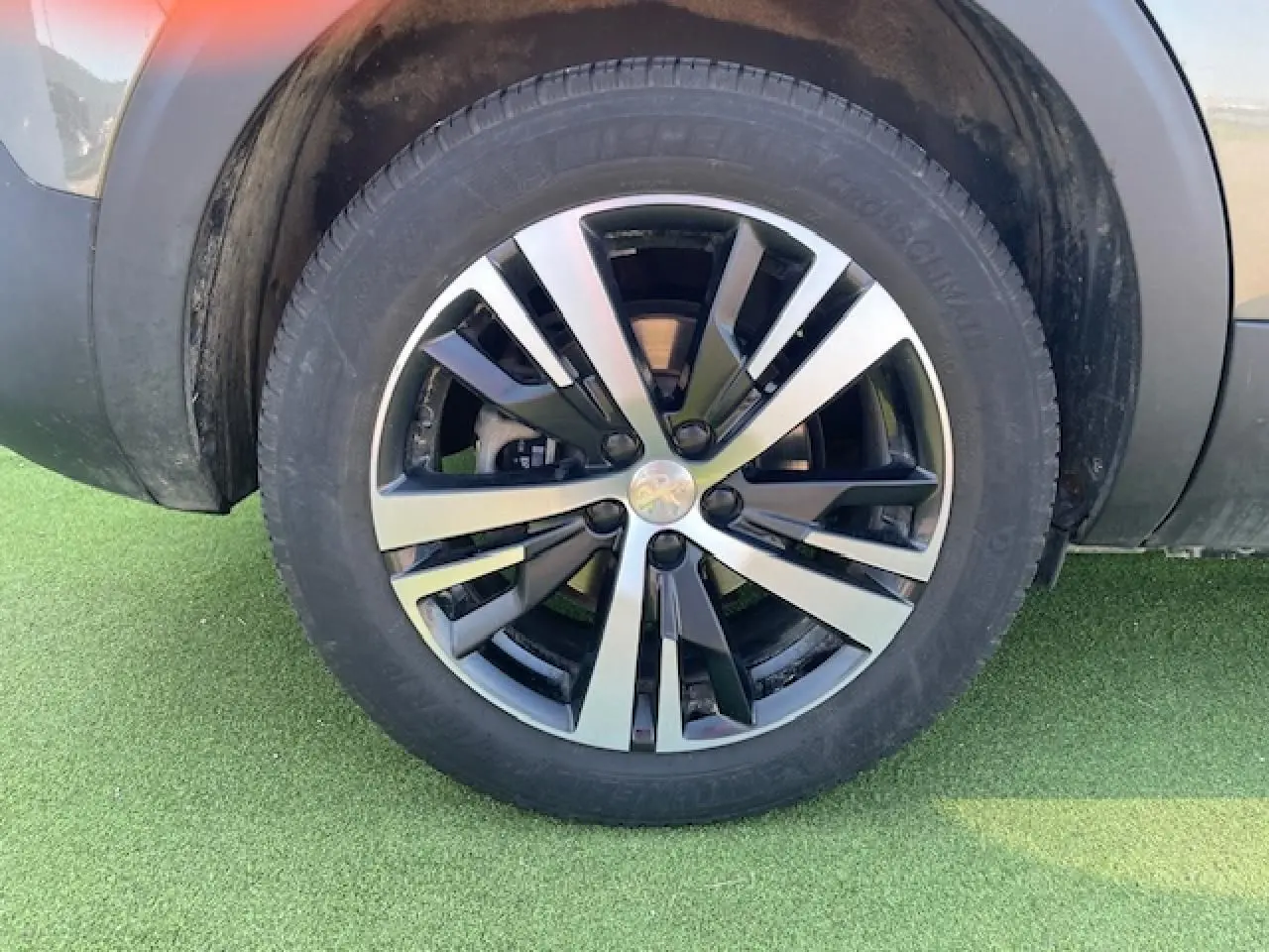 Gros plan sur la roue avant gauche du Peugeot 5008 gris Amazonite avec jante alliage bicolore moderne.