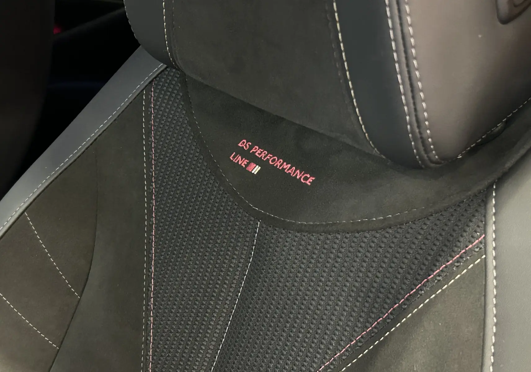 Gros plan sur le siège avant en cuir noir avec surpiqûres rouges et logo DS Performance Line brodé.
