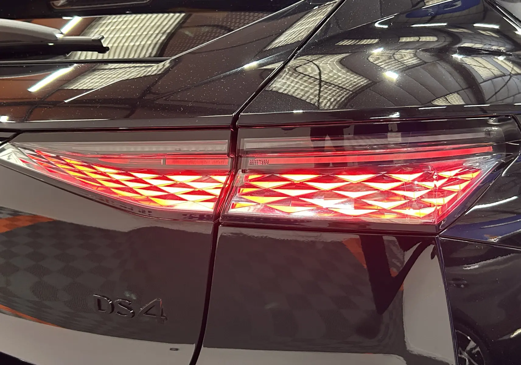 Gros plan sur les feux arrière allumés d'une DS4 noire Perla Nera, mettant en valeur le logo DS4 sur la malle arrière.