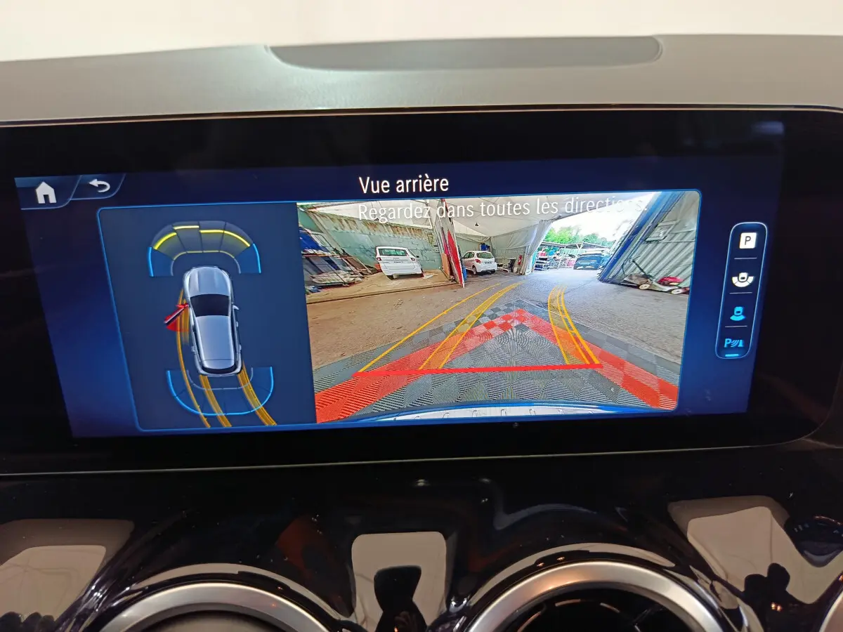 Écran tactile intérieur montrant la caméra de recul et l'aide au stationnement du Mercedes GLA 250 e bleu 2024.