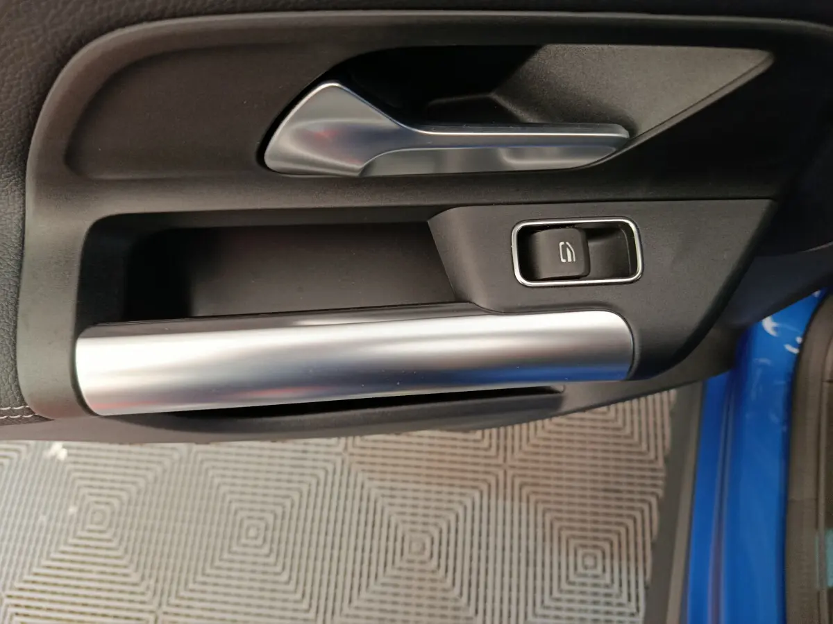 Poignée intérieure côté gauche de porte d'une Mercedes GLA 250 e Business Line bleu, avec bouton de verrouillage noir et garniture argentée.