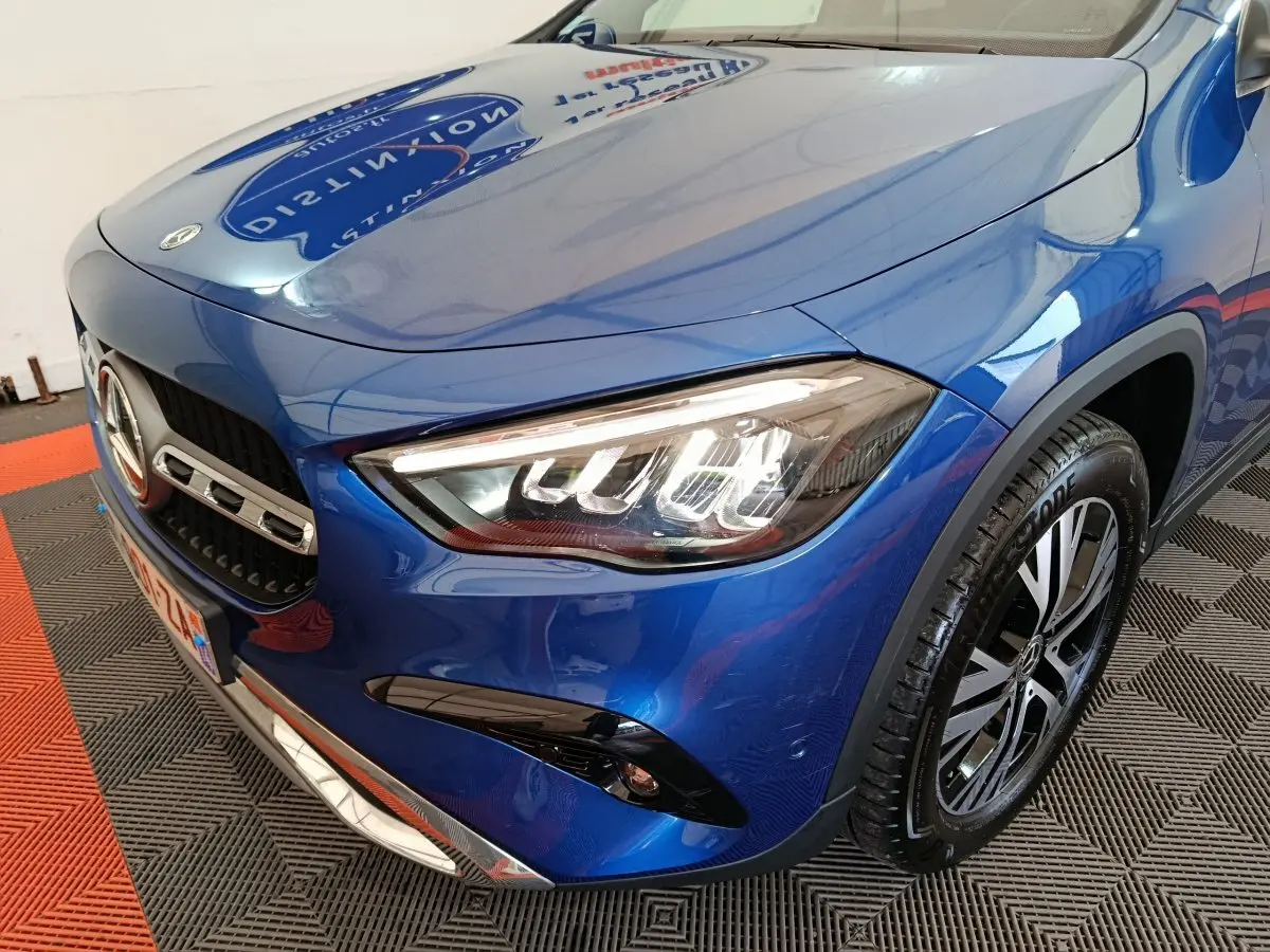 Vue 3/4 avant droit d'une Mercedes GLA 250 e Business Line hybride rechargeable bleu métallisé avec phares LED allumés.