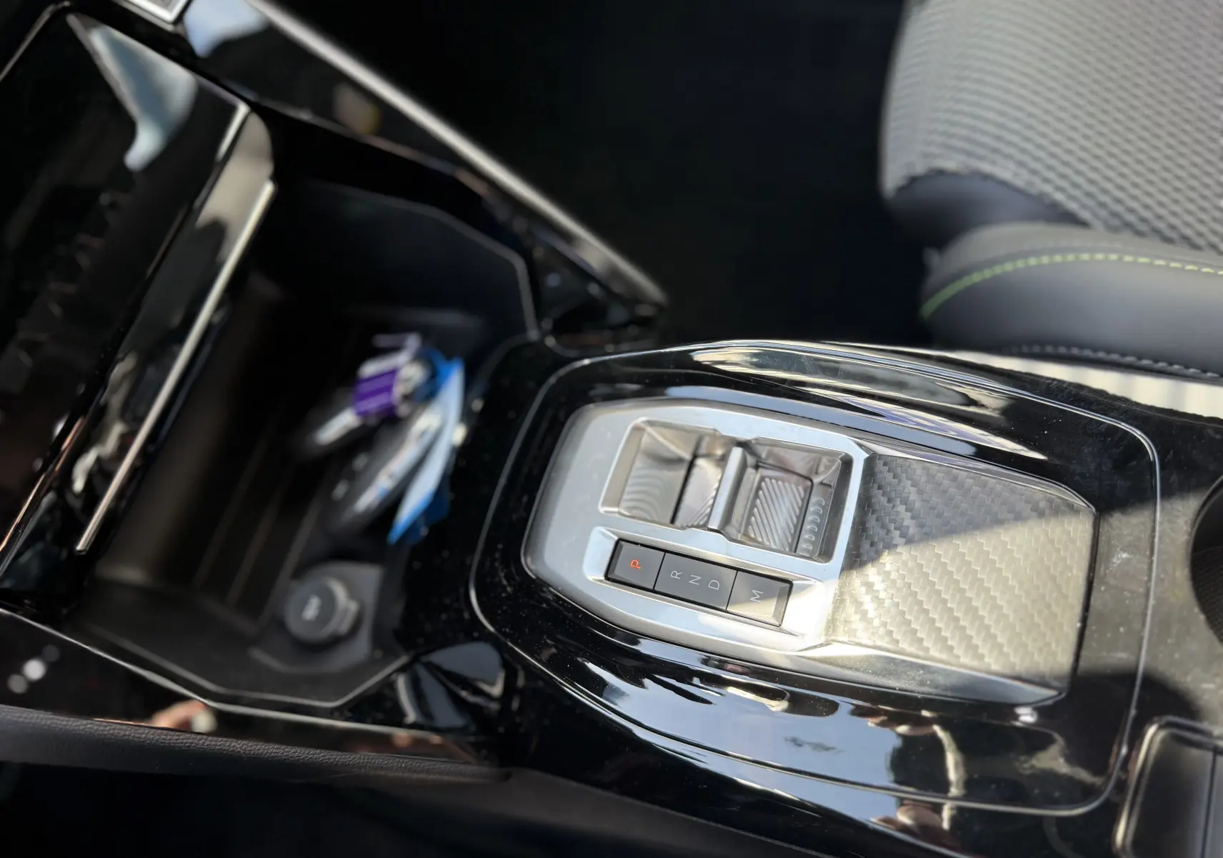 Gros plan sur la console centrale noire brillante du Peugeot 2008 Hybrid 145ch, avec levier de vitesses automatique et surpiqûres vertes sur siège.