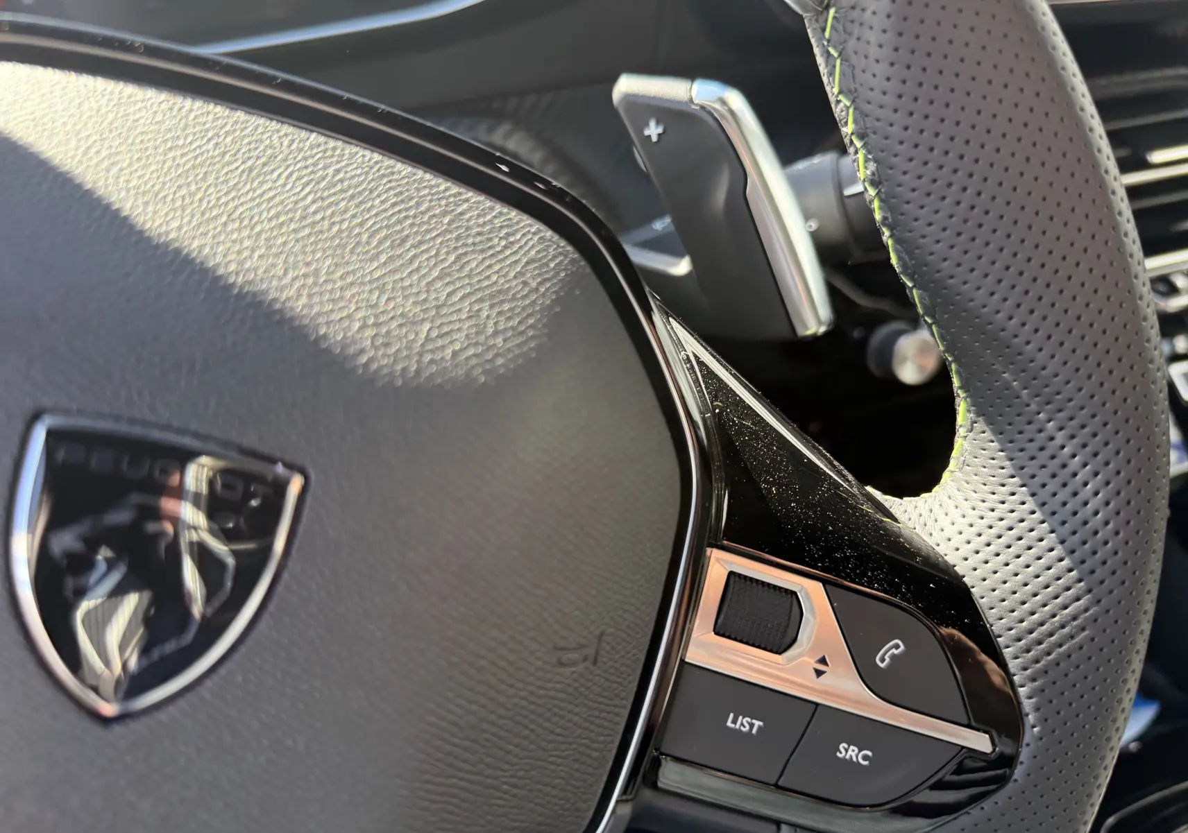 Gros plan sur le volant perforé noir du Peugeot 2008 Hybrid 145ch, avec commandes intégrées et palettes au volant.