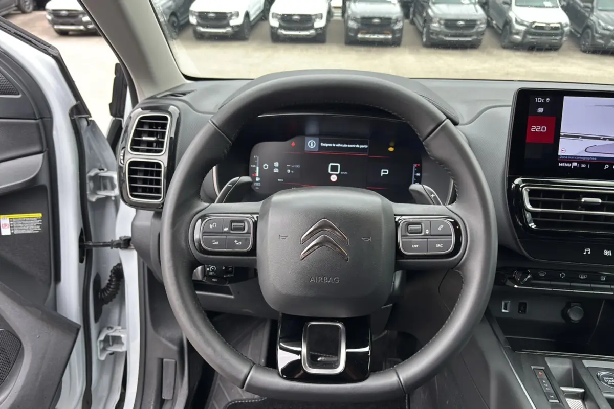 Vue intérieure centrée sur le volant cuir multifonctions du Citroën C5 Aircross Hybrid blanc, avec tableau de bord digital et écran tactile.