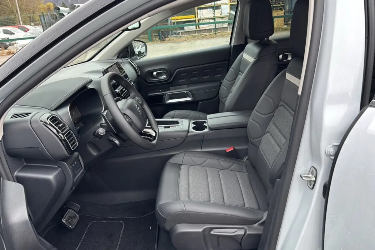 Vue intérieure côté conducteur du Citroën C5 Aircross Hybrid blanc, montrant les sièges en cuir et tissu gris et le tableau de bord moderne.
