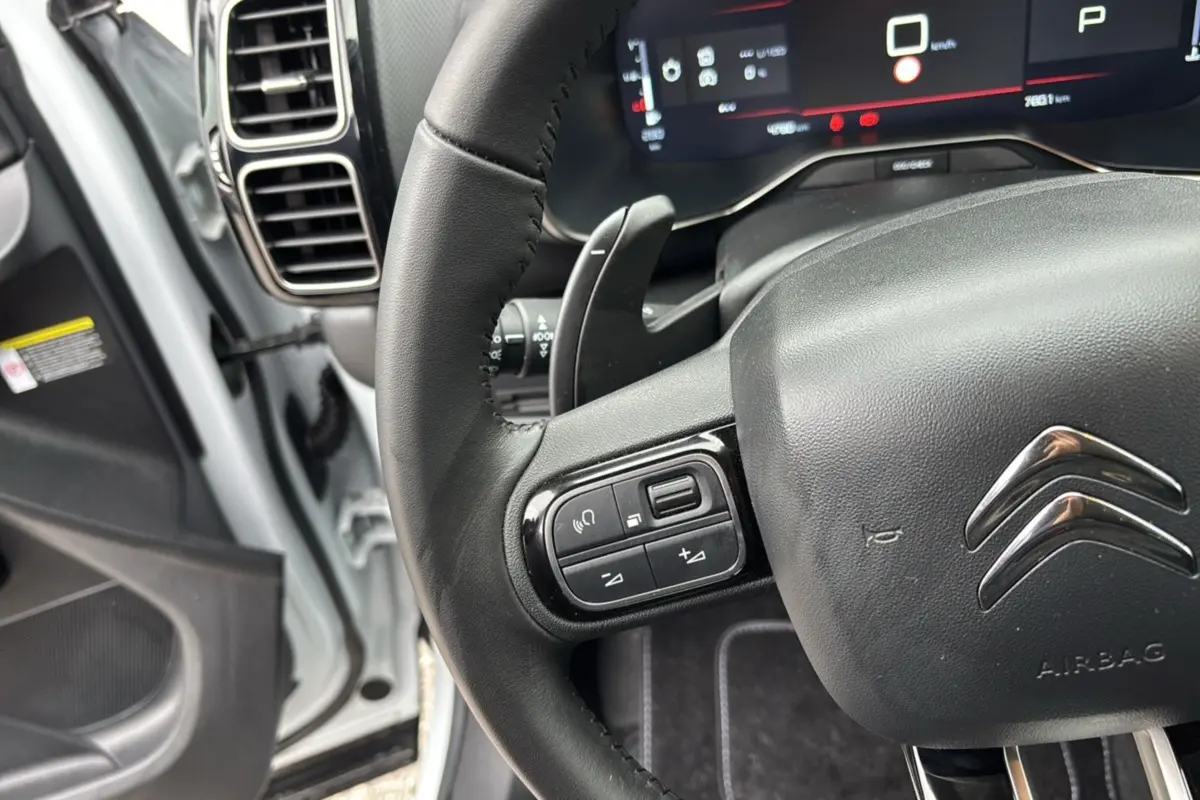 Gros plan sur le volant cuir multifonctions de la Citroën C5 Aircross Hybrid 145, avec tableau de bord numérique en arrière-plan.