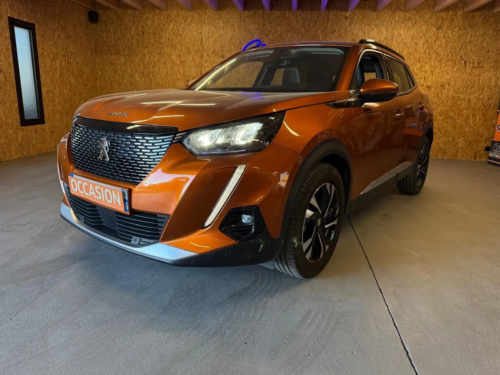 Peugeot 2008 orange vue 3/4 avant droit avec calandre noire et feux LED allumés en intérieur.