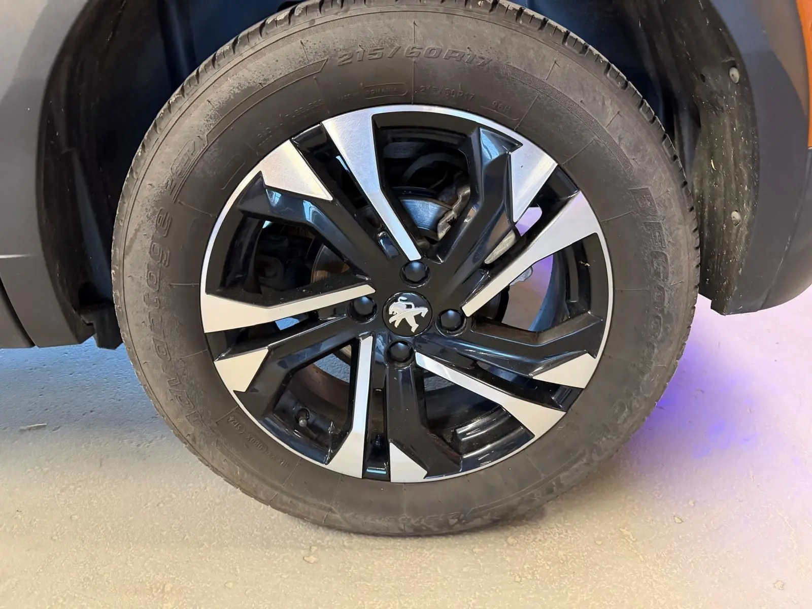 Gros plan sur la jante alliage 17'' bi-ton noir et argent avec logo Peugeot au centre du Peugeot 2008 orange.