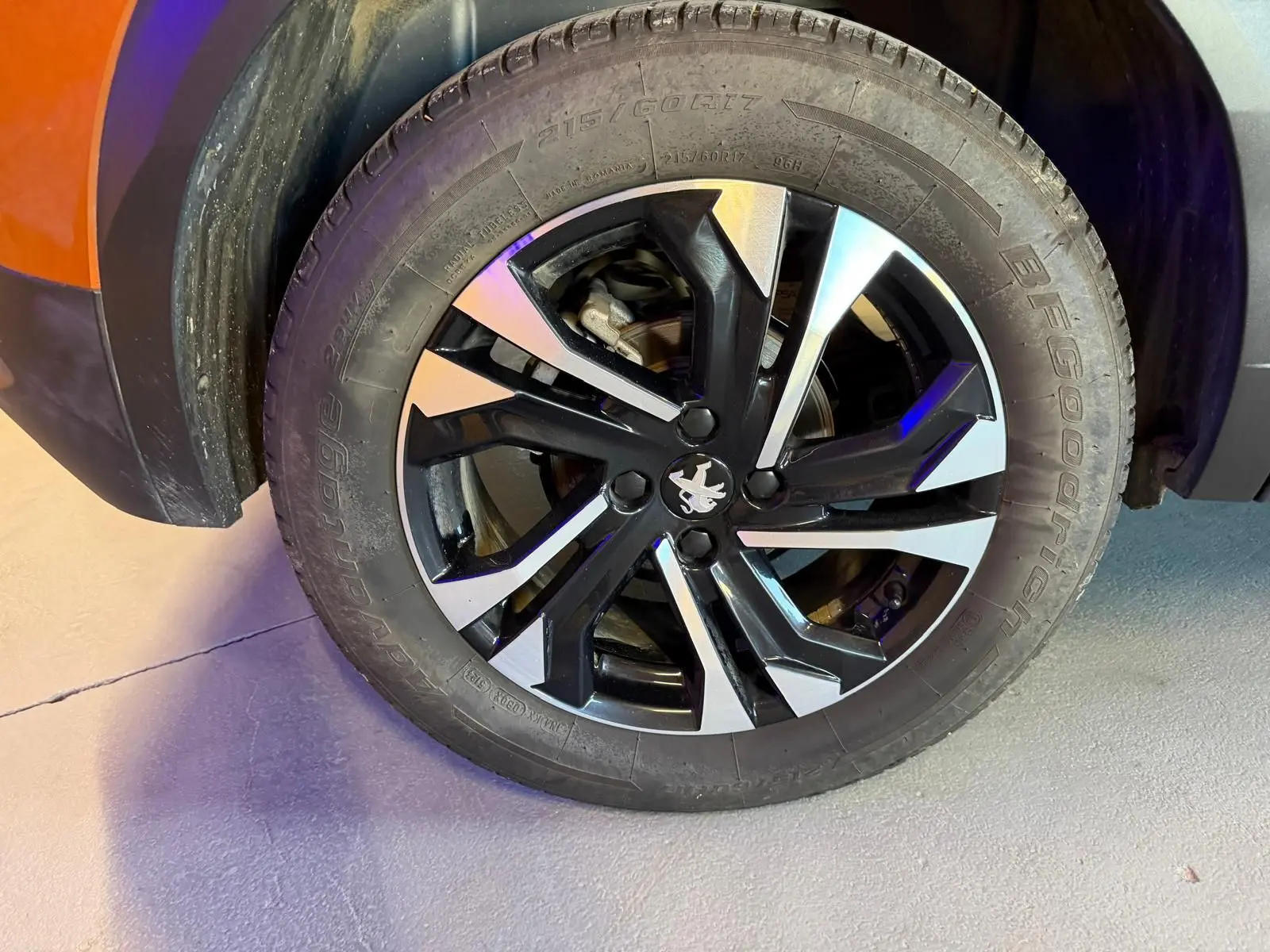 Gros plan sur la roue avant gauche d’un Peugeot 2008 orange, jante alliage bi-ton noir et argent avec logo lion central.