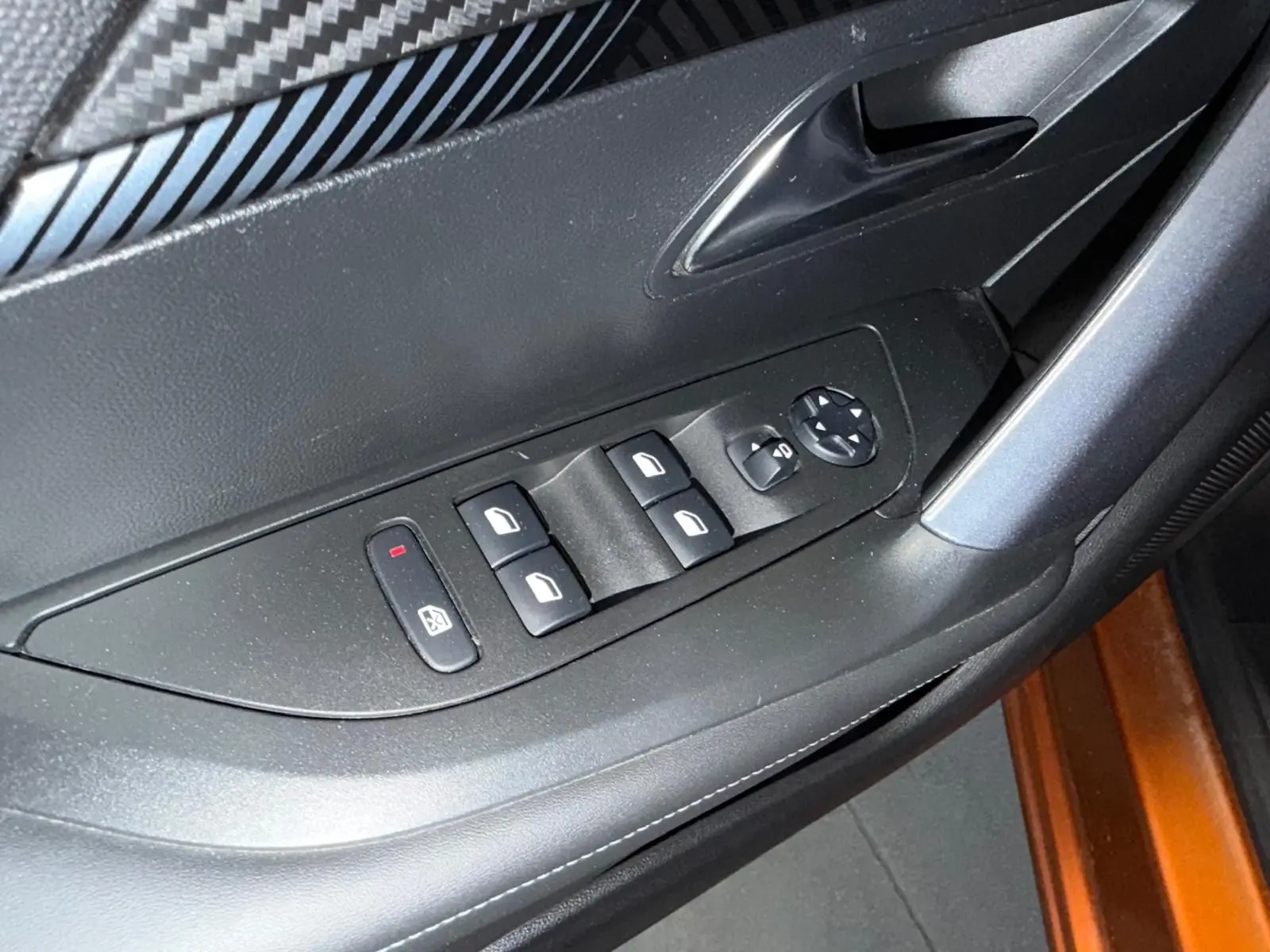 Gros plan sur la commande des vitres électriques côté conducteur dans l'intérieur noir du Peugeot 2008 orange 2020.