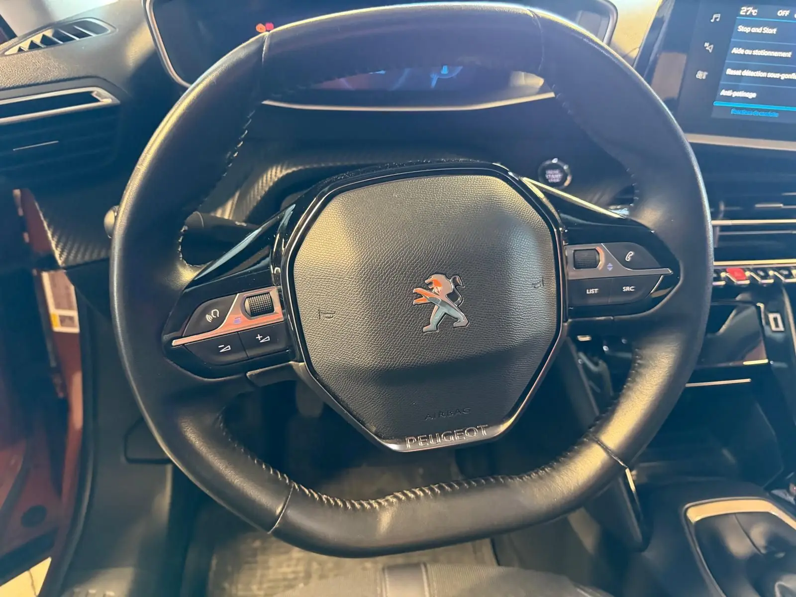 Vue rapprochée du volant compact en cuir noir avec logo Peugeot, tableau de bord et console centrale du 2008 orange 2020.