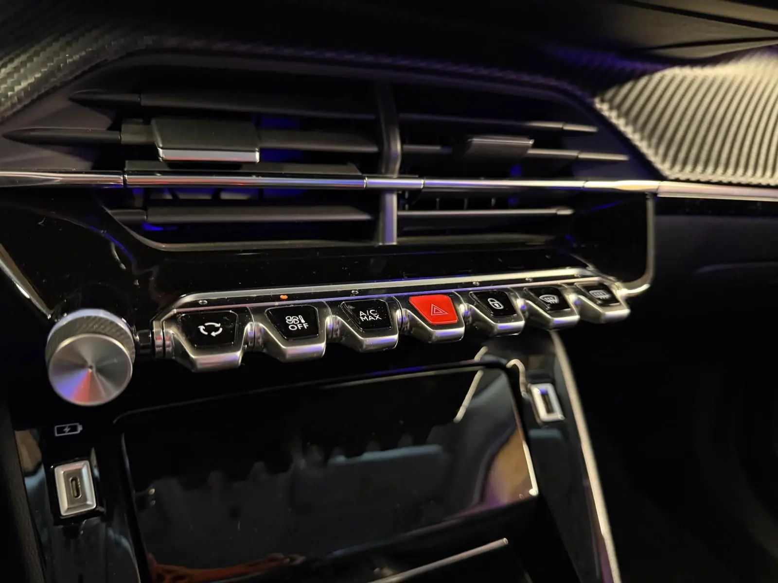 Gros plan sur la console centrale noire brillante du Peugeot 2008 1.5 BlueHDi 100 Allure avec boutons chromés et bouton rouge d'alerte.