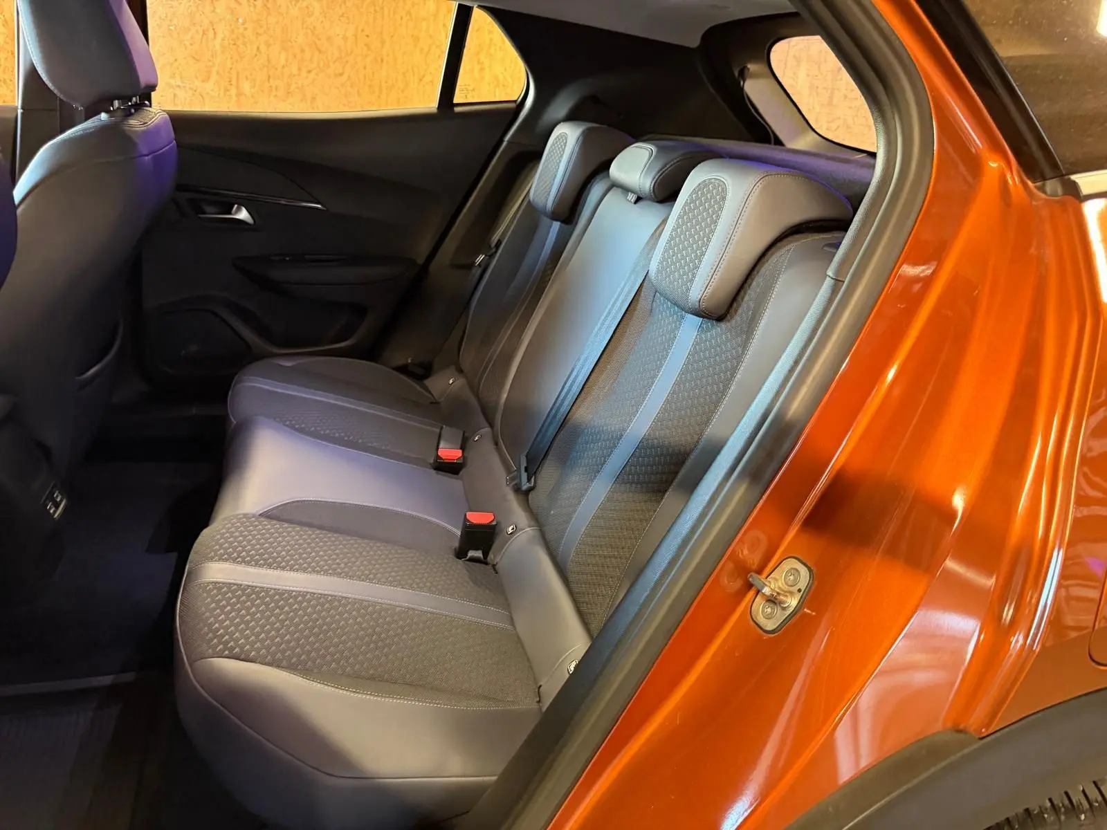 Vue intérieure côté droit sur la banquette arrière grise du Peugeot 2008 orange métallisé avec ceintures de sécurité visibles.