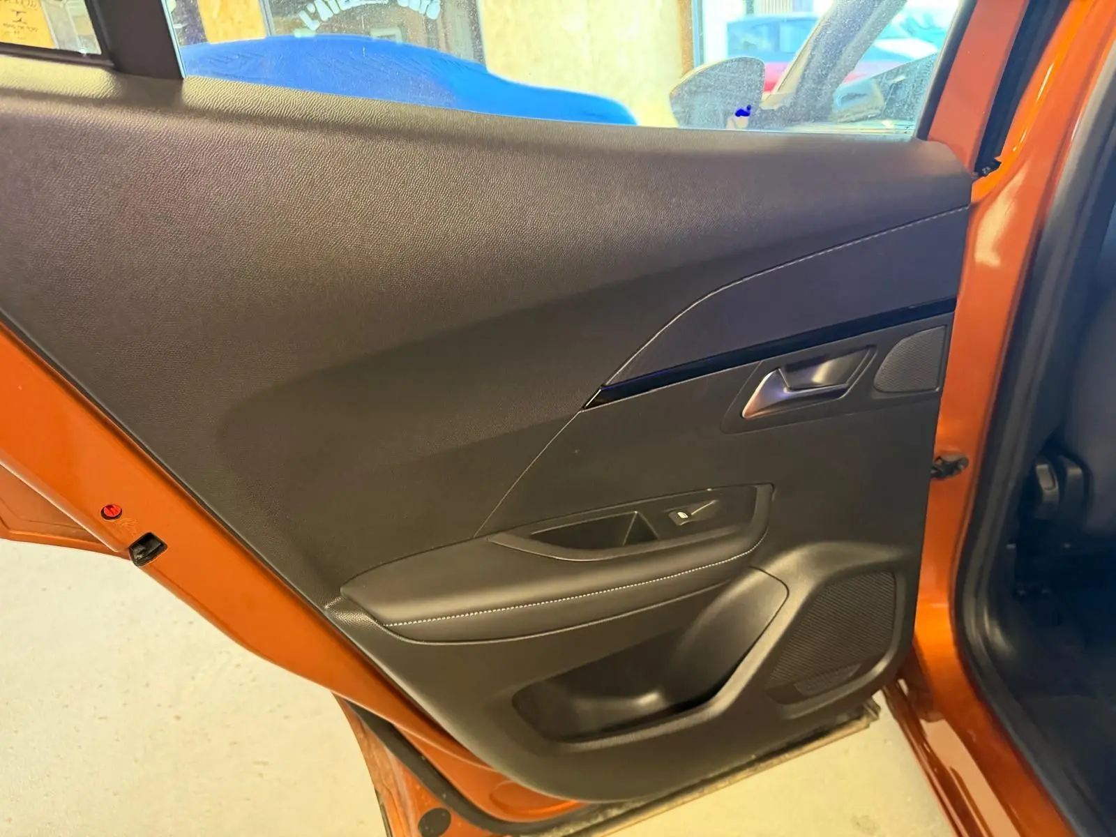 Vue intérieure de la porte arrière gauche orange du Peugeot 2008 1.5 BlueHDi 100 Allure avec garniture noire et commande de vitre.