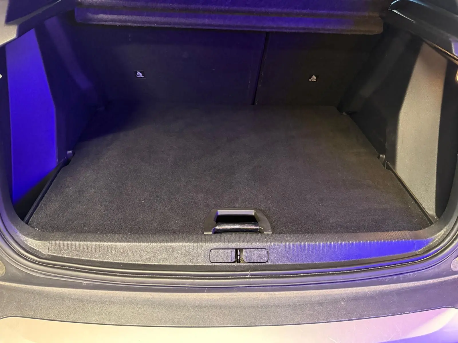 Coffre ouvert vu de l'arrière d'un Peugeot 2008 orange, espace de chargement vide et tapis noir.