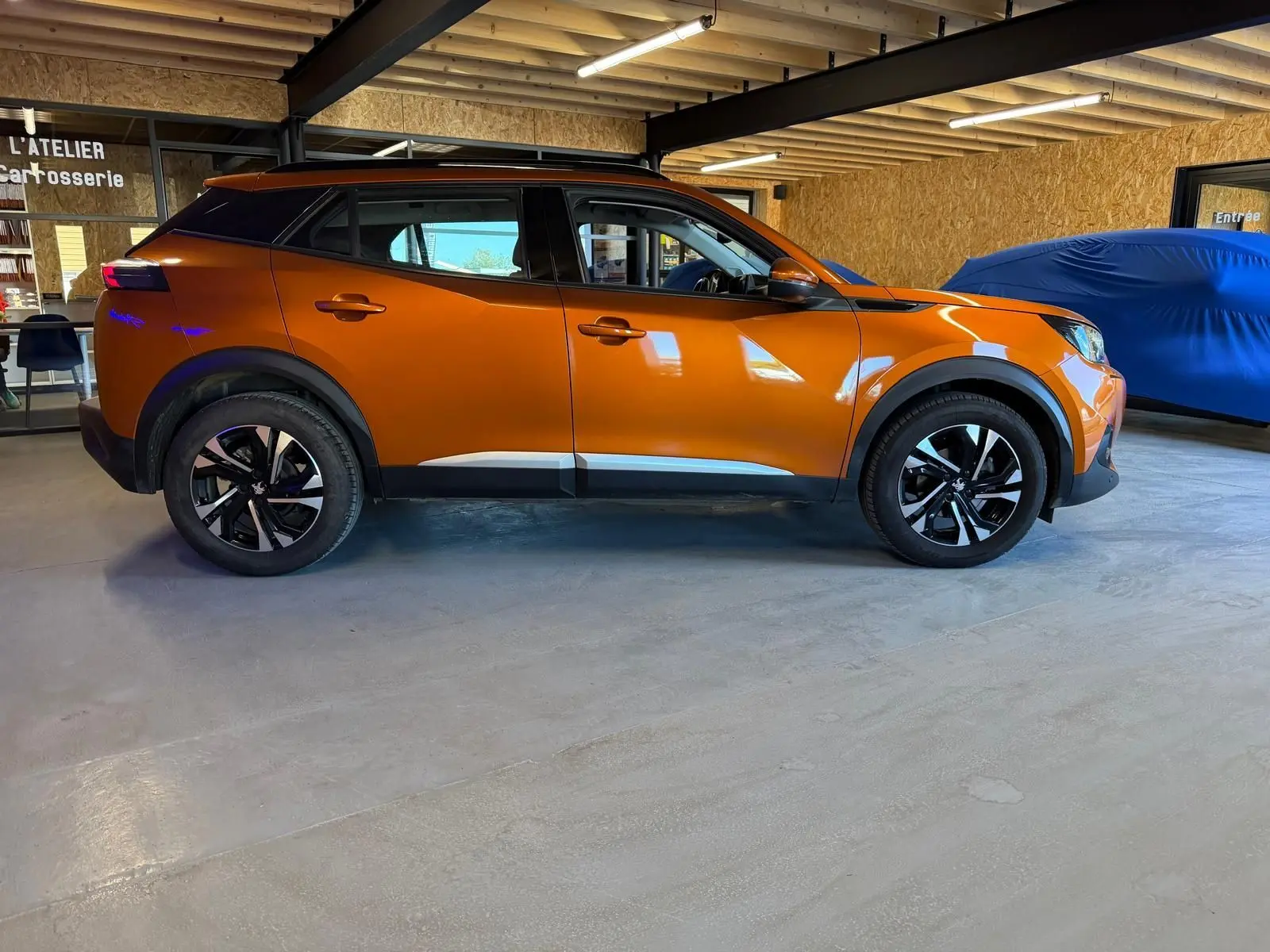 Peugeot 2008 orange vue de profil côté gauche, avec jantes alliage bi-ton et barres de toit noires.