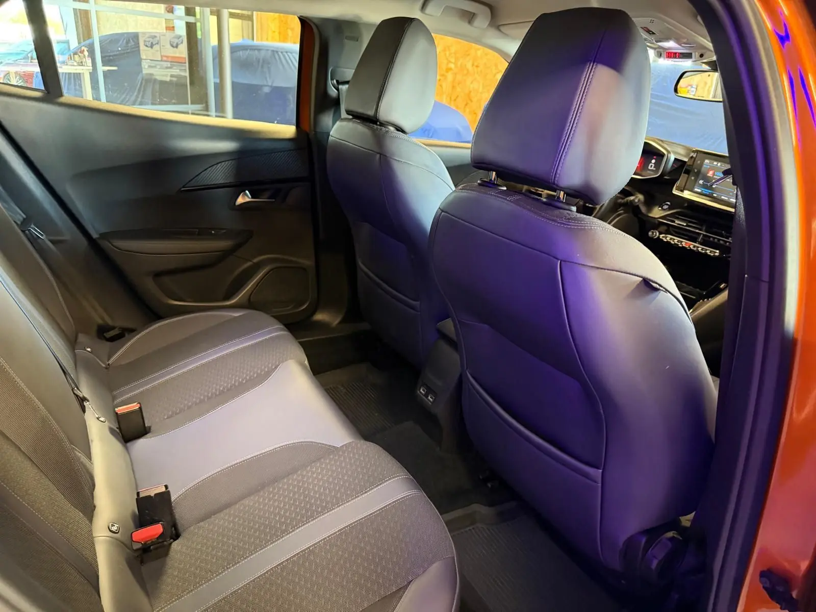 Vue intérieure arrière droite du Peugeot 2008 orange 2020, montrant la banquette 1/3-2/3 et les sièges avant en tissu gris.