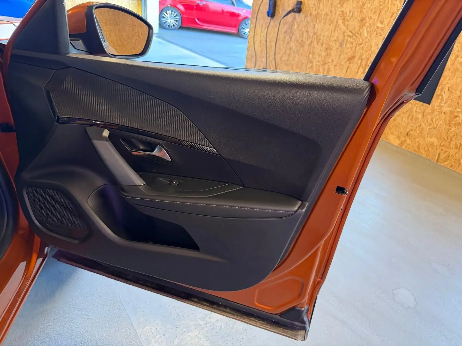 Vue intérieure de la porte avant gauche orange du Peugeot 2008 1.5 BlueHDi avec insert carbone et poignée chromée.