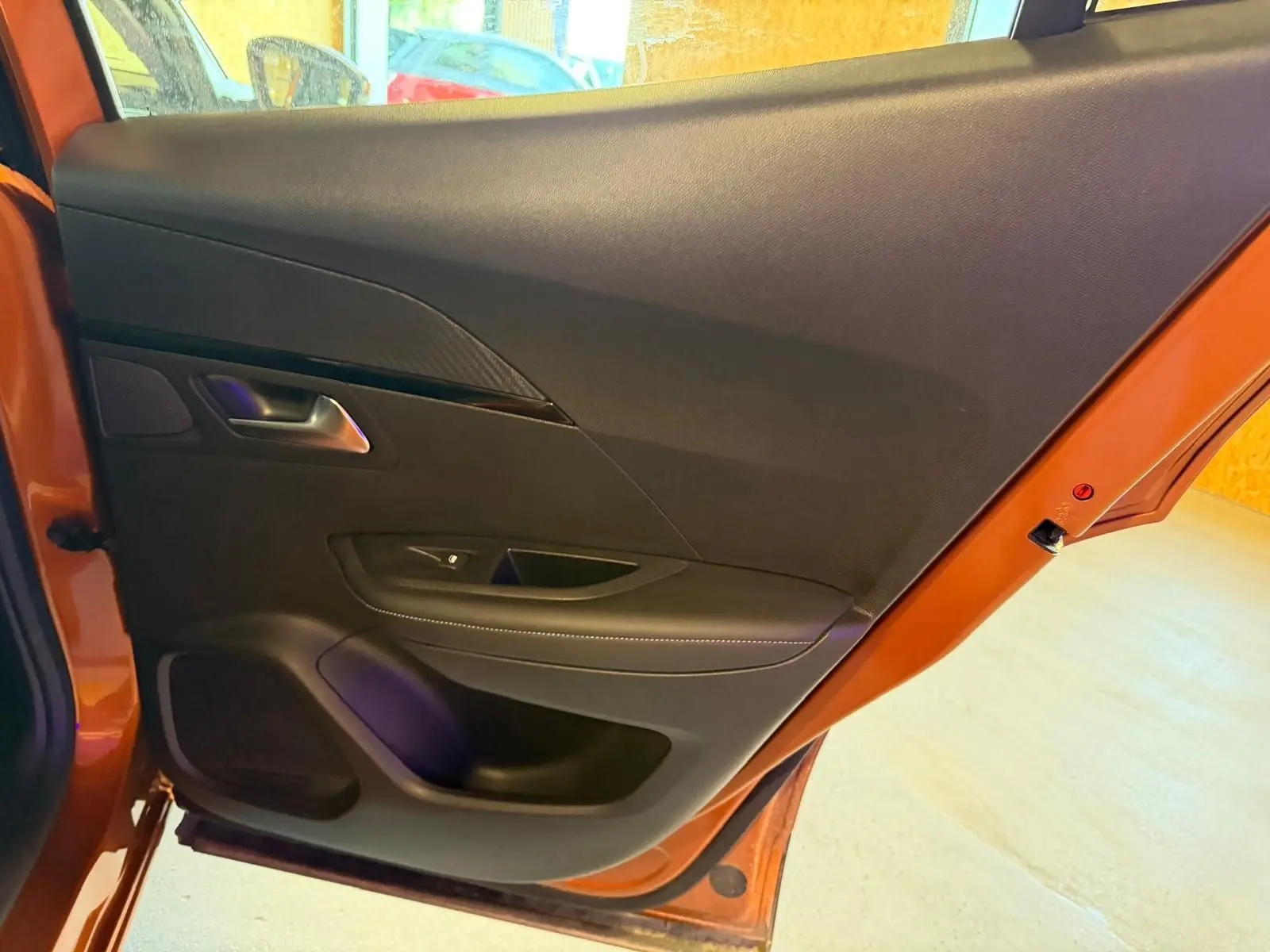 Vue intérieure de la porte arrière gauche orange du Peugeot 2008 2020 avec garniture noire et poignée métal.