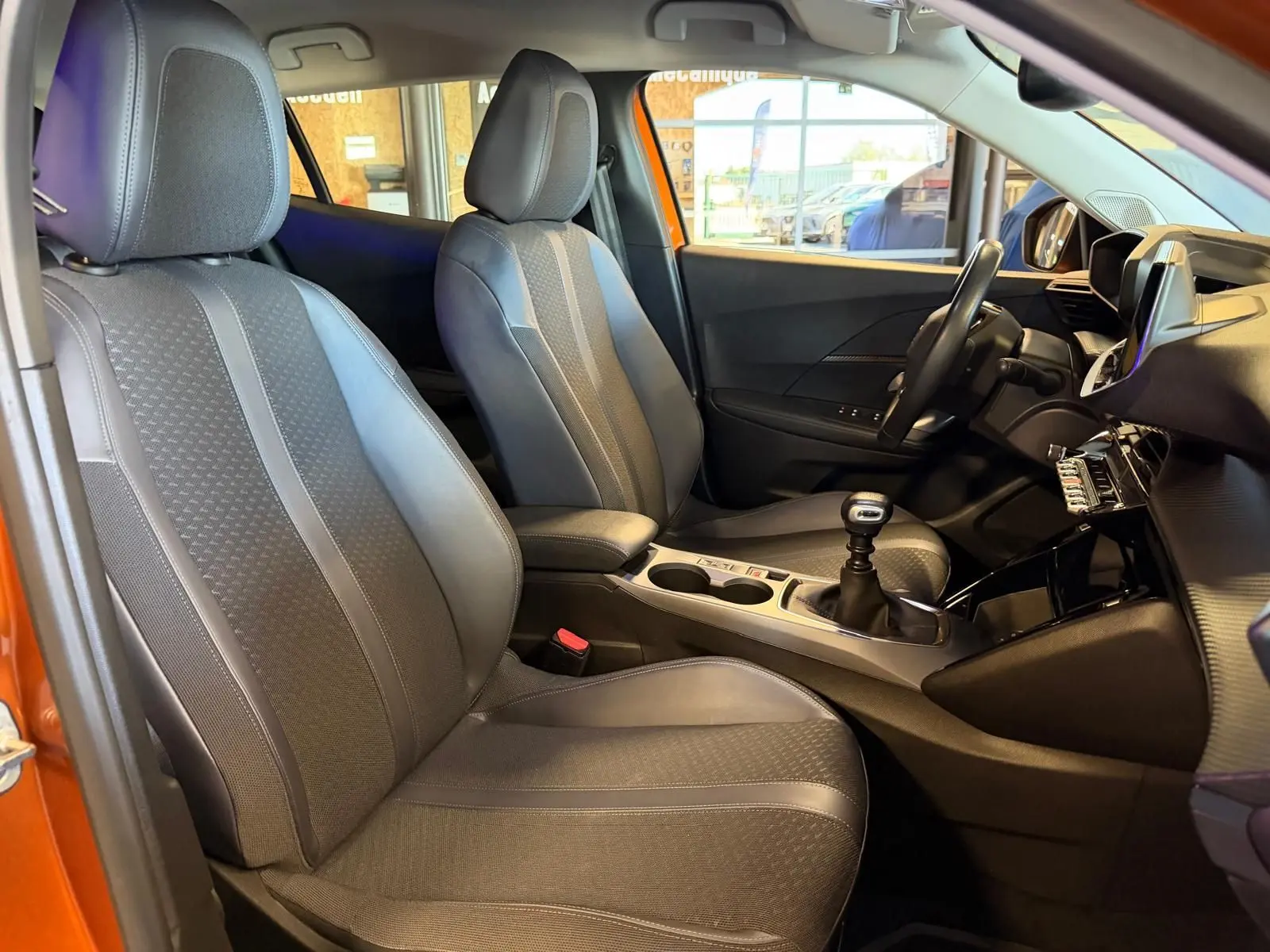Vue intérieure côté gauche du Peugeot 2008 orange, montrant sièges tissu gris et levier de vitesse manuel.