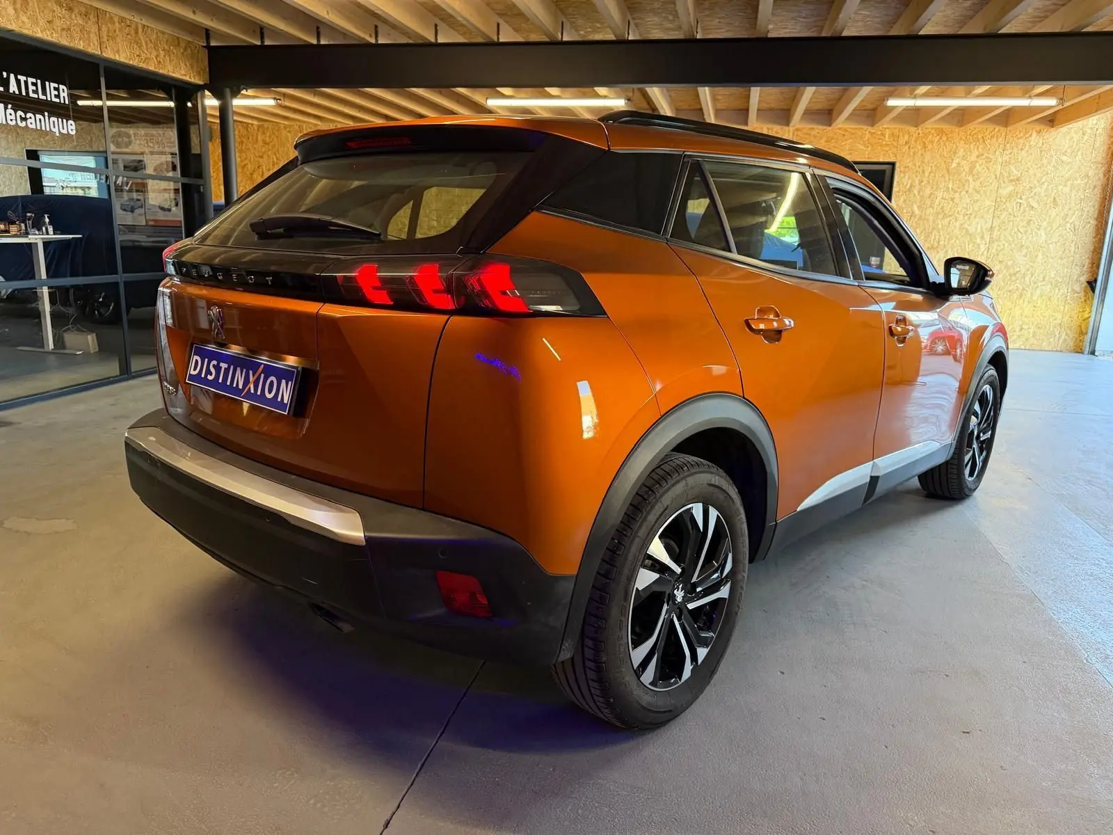 Vue 3/4 arrière droite d’un Peugeot 2008 orange métallisé avec feux arrière LED en forme de griffes et jantes alliage bi-ton.
