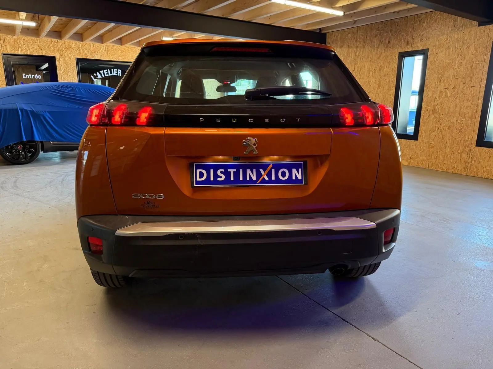 Vue arrière d'un Peugeot 2008 orange avec feux LED en forme de griffes et plaque Distinxion visible en intérieur.